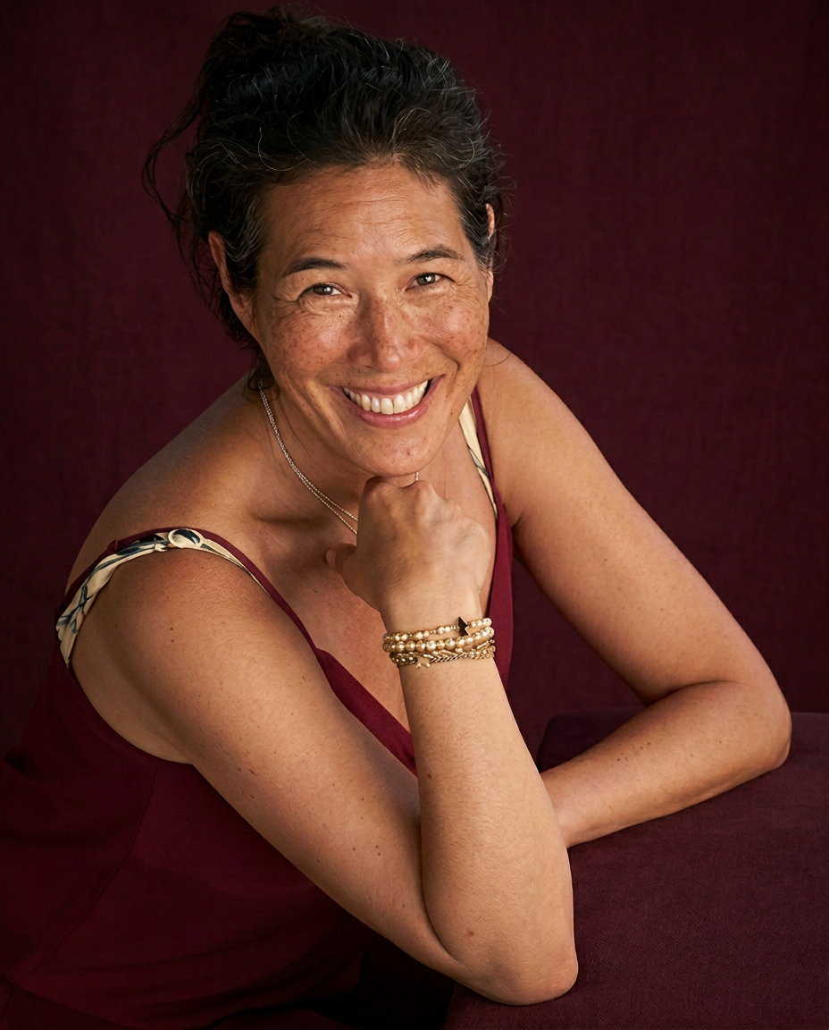 Marjolein smiling with her chin resting on her hand, wearing bordeaux with narrow patterned straps with gold details and gold bracelets